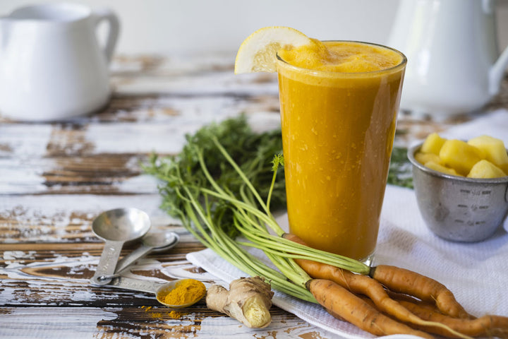 Turmeric smoothie in clear glass with fresh carrots, ginger, pineapple and Two Roots Turmeric powder