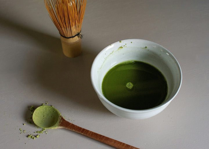 bright green matcha green tea powder with wooden spoon and whisk