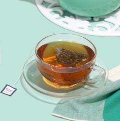 Clear glass cup with tea and a tea bag on a light green background