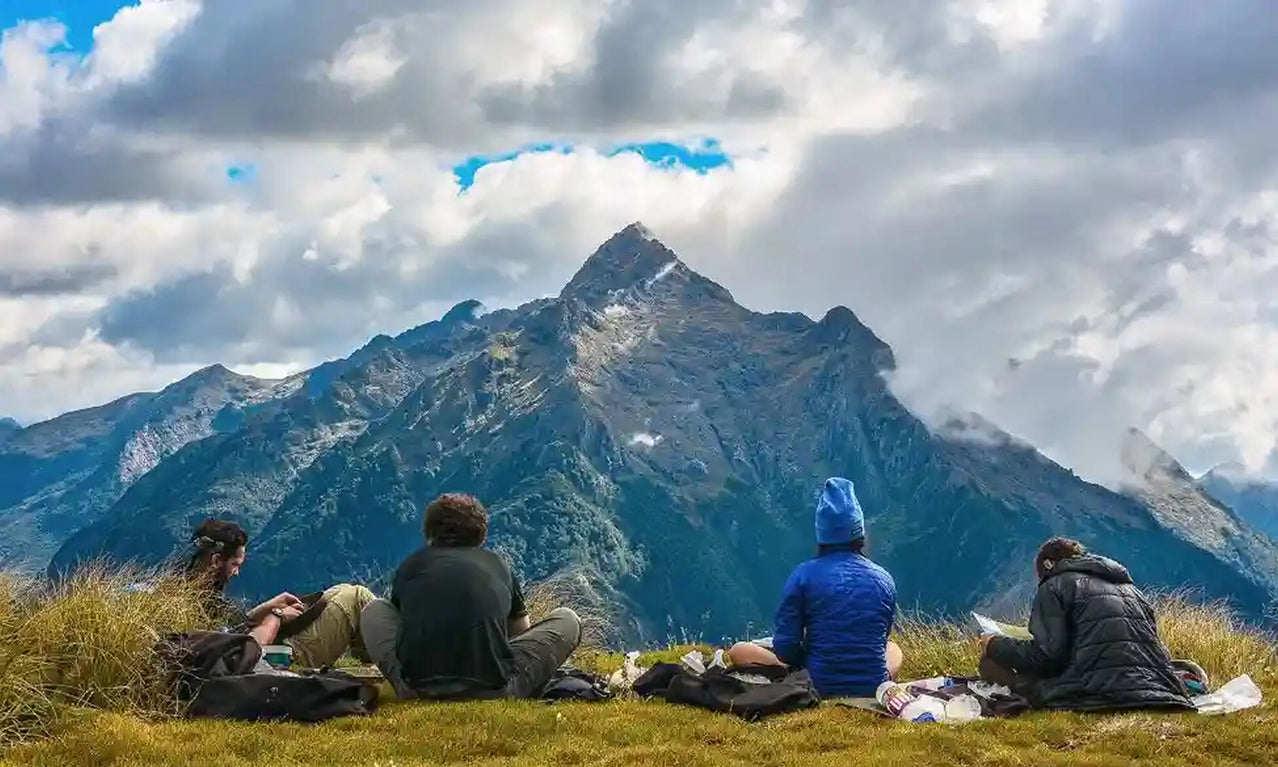 Four people sitting on a grassy hilltop with mountains in the background