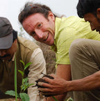 Three people outdoors, two of whom are planting a small plant.