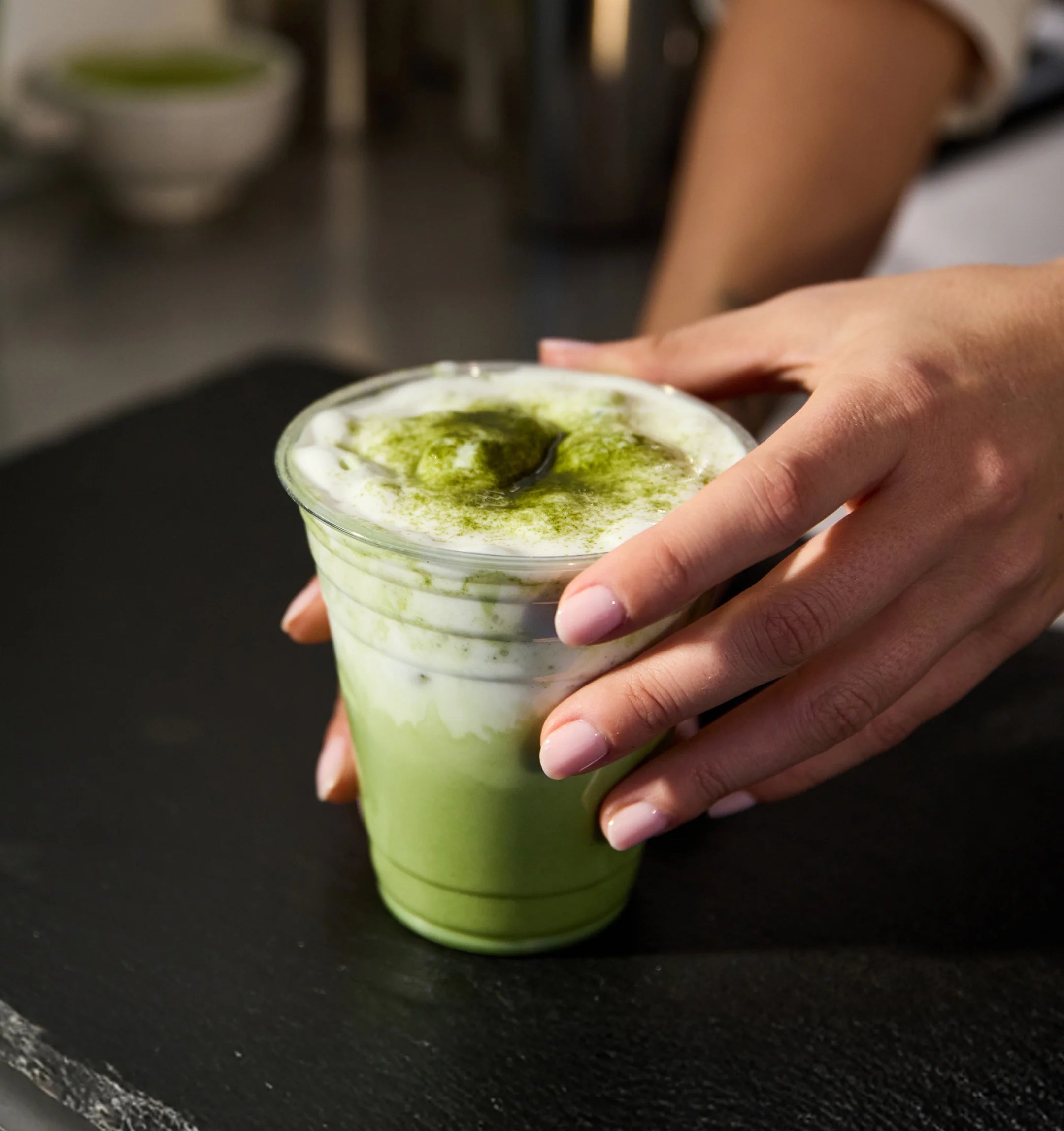 Person holding a cup of green matcha latte on a dark surface