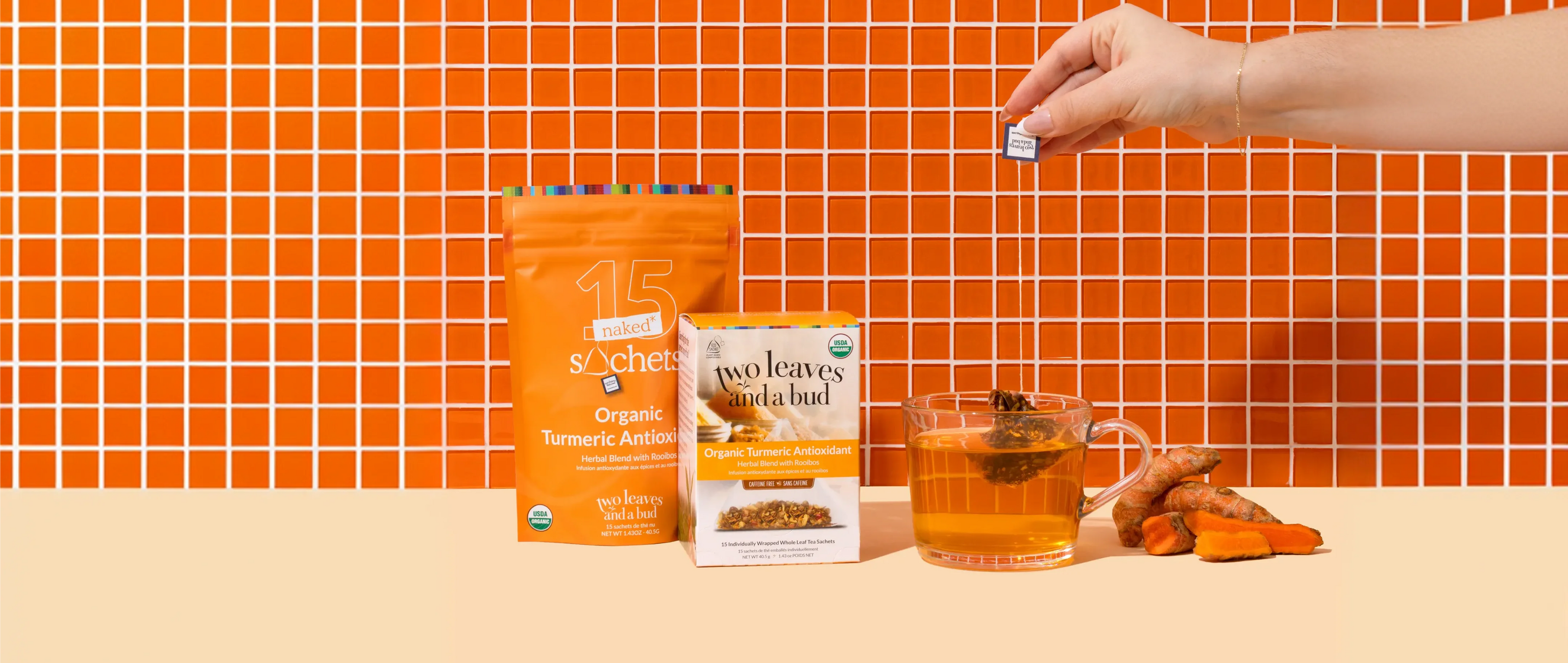Two Leaves and a Bud tea packaging with a cup of tea and tea leaves on an orange tiled background.