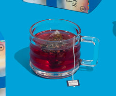 Clear glass mug with red tea and a tea bag on a blue background