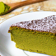 Slice of green matcha cake with powdered sugar on a white plate