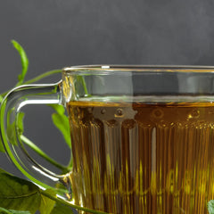 Clear glass mug filled with amber liquid, likely tea, with green leaves on a dark background