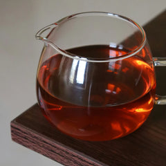 Glass teapot filled with red liquid on a wooden coaster