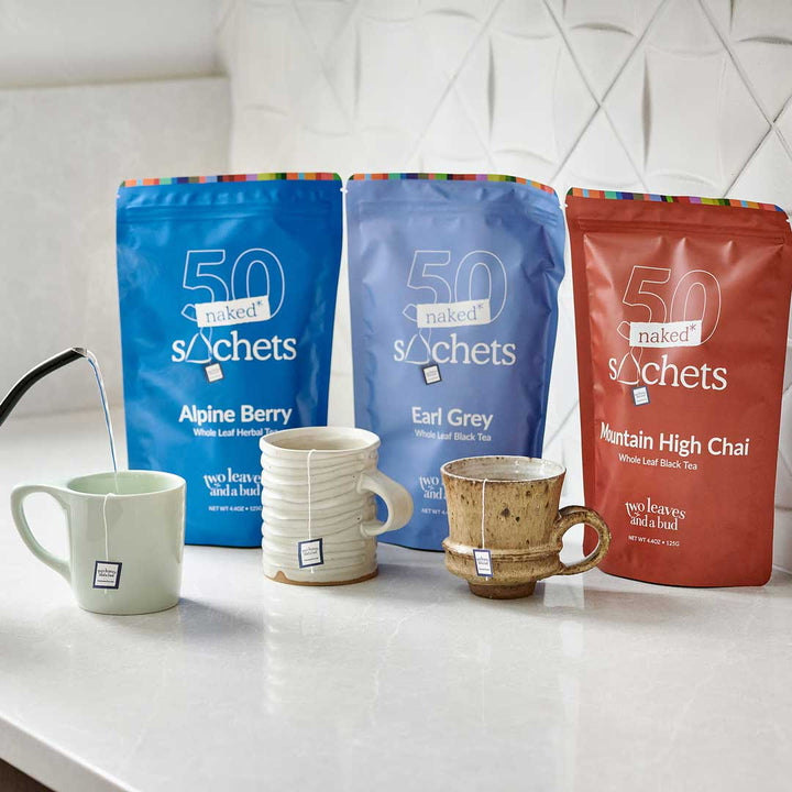 Sleeves of tea sachets on countertop with three tea mugs