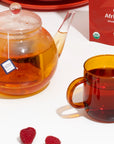 Tea set with a teapot, mug, and box of Organic African Sunset tea on a white surface.