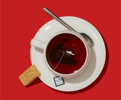 Tea cup with saucer, spoon, tea bag, and cracker on a red background