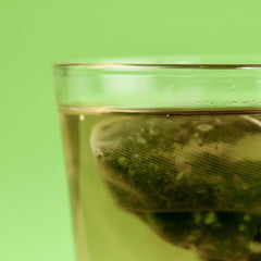 Tea bag in a glass of water against a green background