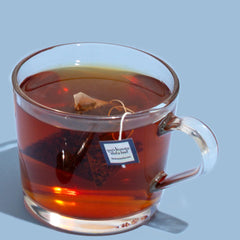 Clear glass mug filled with hot tea on a light blue background