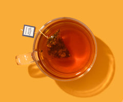 Clear glass mug filled with tea on a yellow background